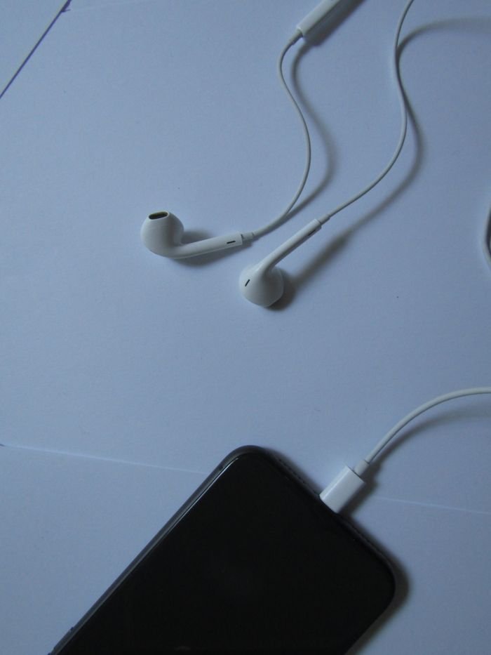 Minimalist photo of a smartphone with white earphones on a light background, plugged in and ready to use.