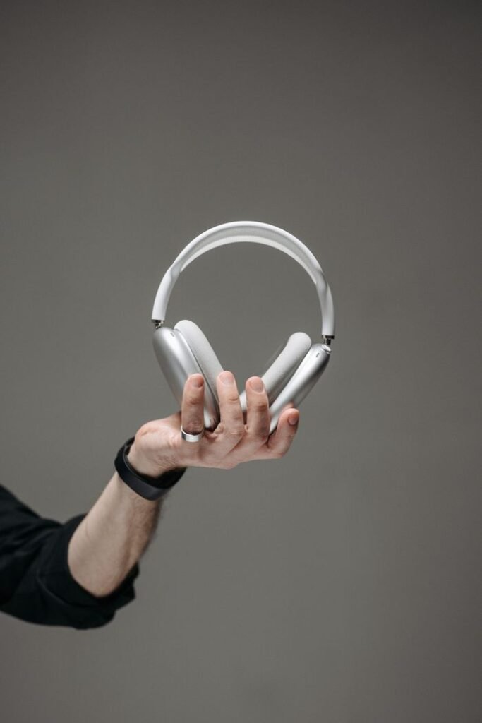 Close-up of a hand holding sleek wireless headphones against a gray backdrop.